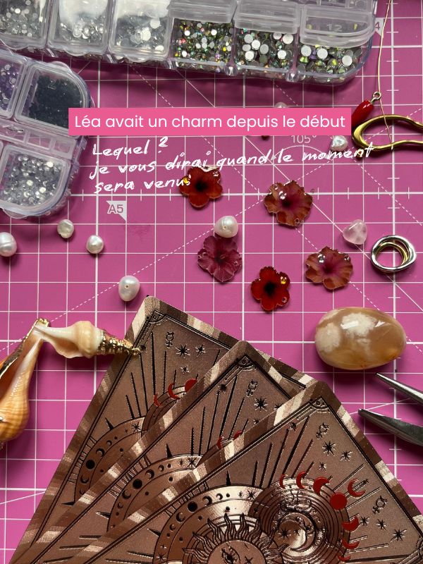 backstage atelier avec les charms lodzé et des cartes de tarot. Texte "Léa avait un charm depuis le début. Lequel ? Je vous le dirai quand le moment sera venu"