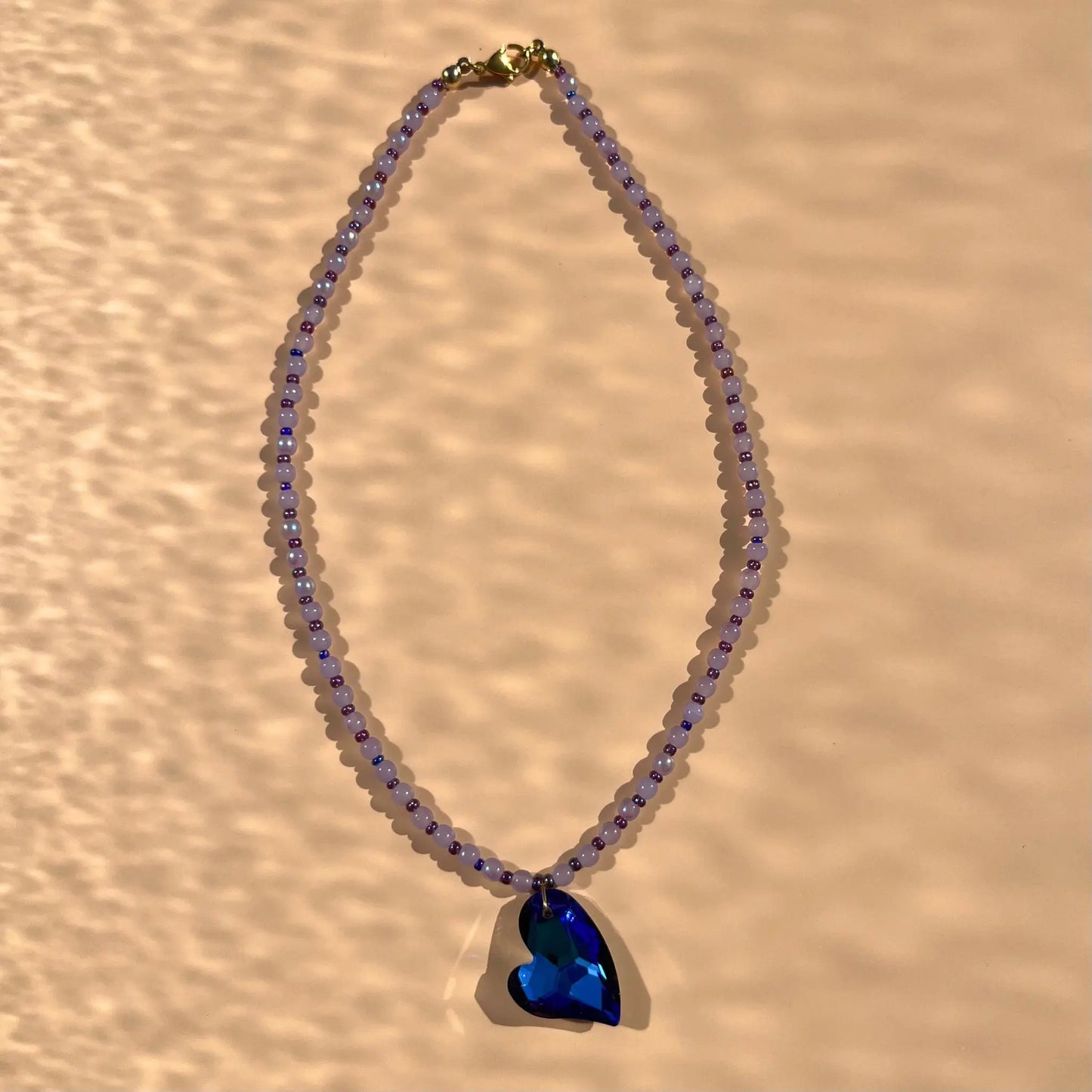 Collier avec un pendentif en verre bleu profond, et une alternance de perles parme et perles de rocaille violettes upcyclées