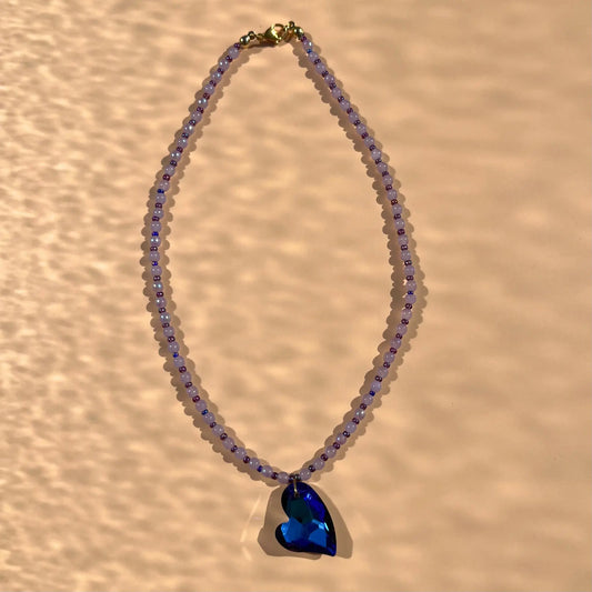 Collier avec un pendentif en verre bleu profond, et une alternance de perles parme et perles de rocaille violettes upcyclées
