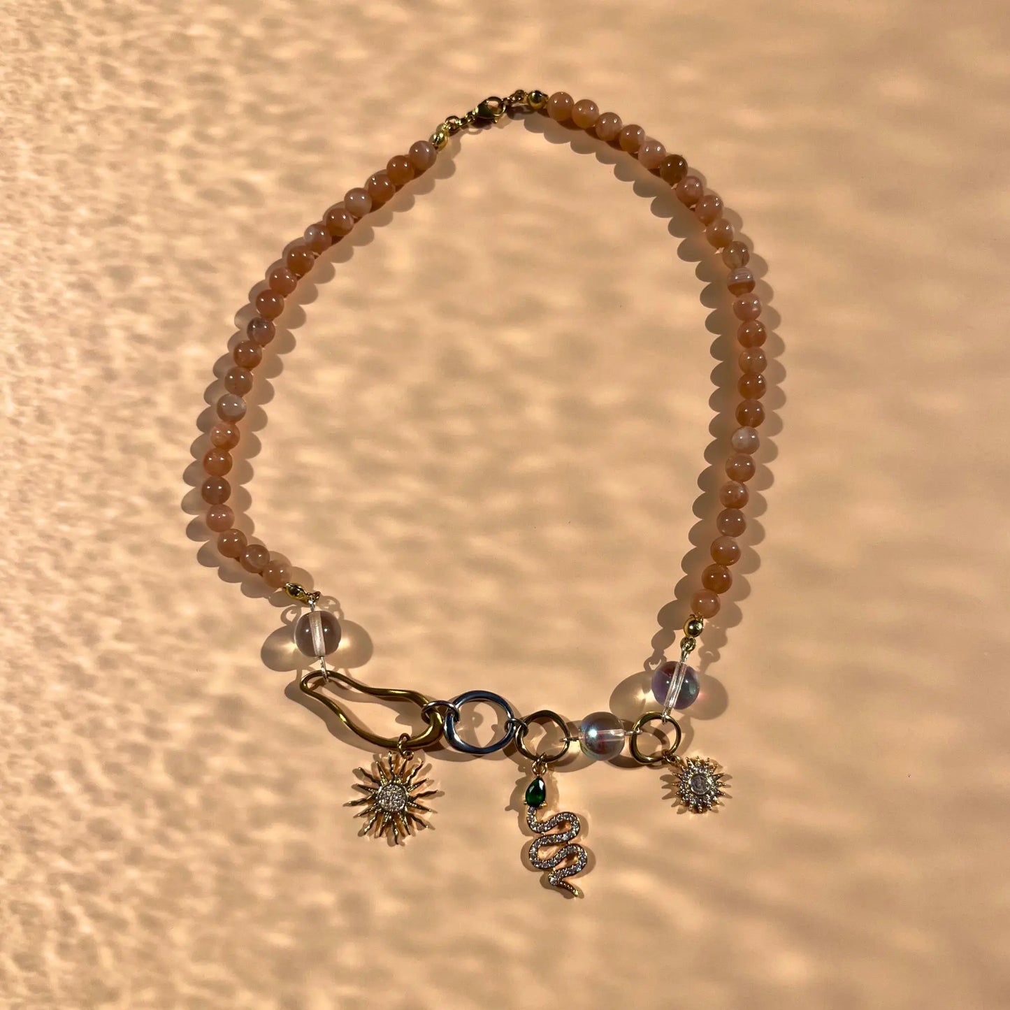 Collier en perles de soleil et trois charms : deux soleils et un serpent, montés sur des formes organiques en acier inoxydable