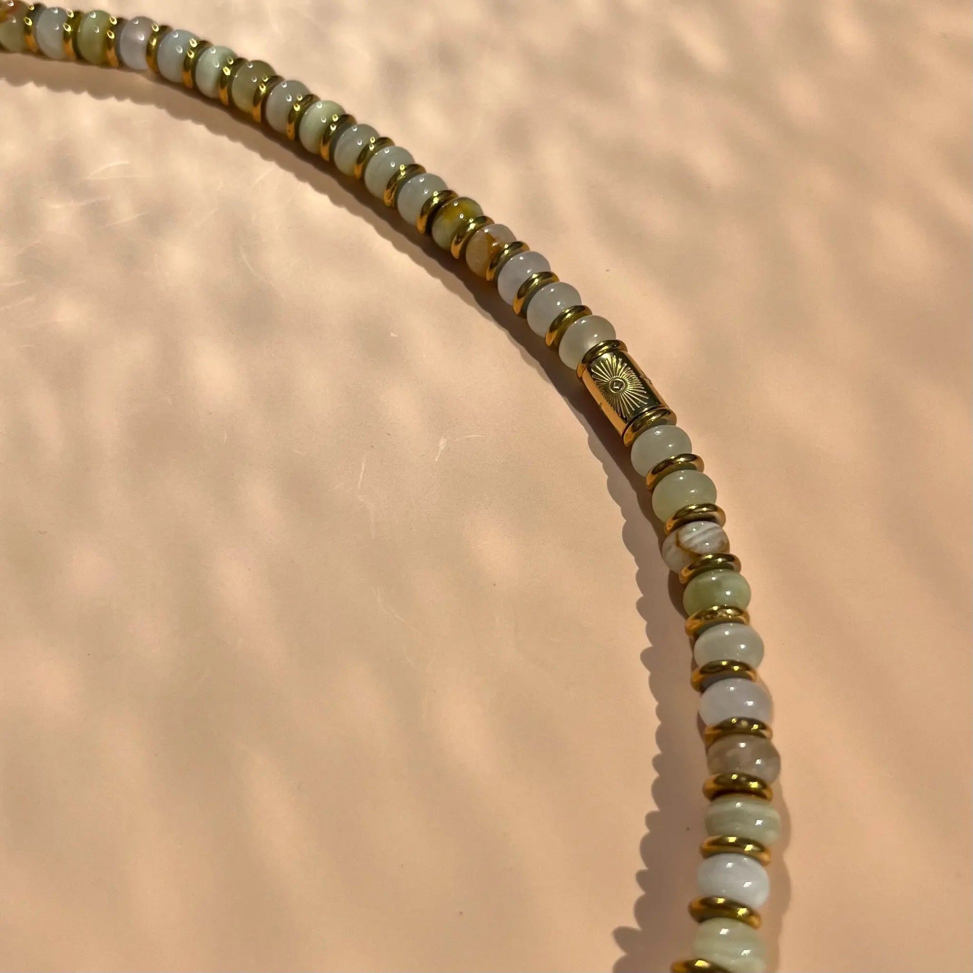 zoom sur collier en disque de jade et d'hématie, détail perle tube plaqué or motif oeil protecteur